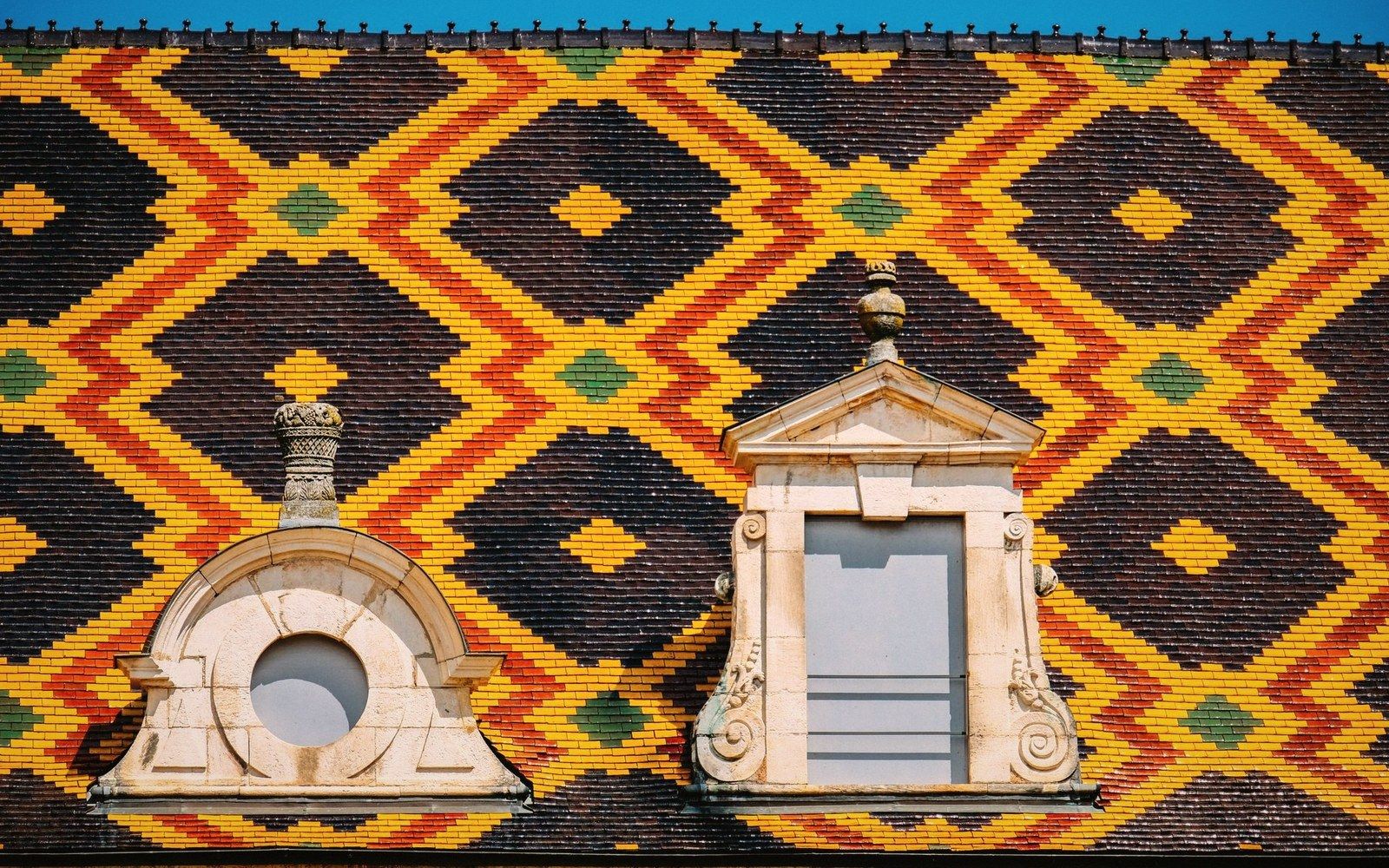 Colorful geometric patterned tile roof with two ornate stone dormer windows in Beaune