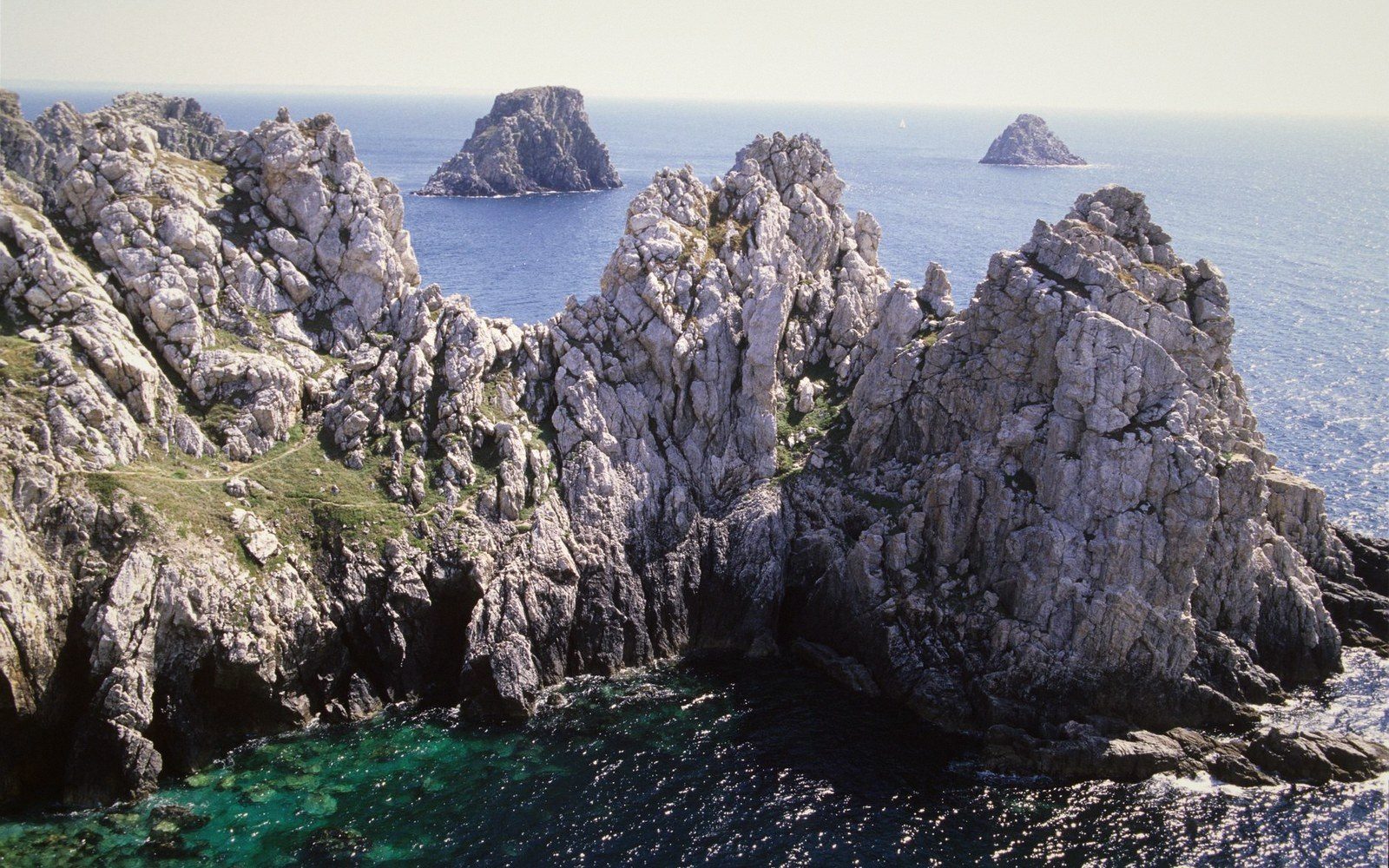 Jagged cliffs jut into turquoise water with rocky islets visible offshore