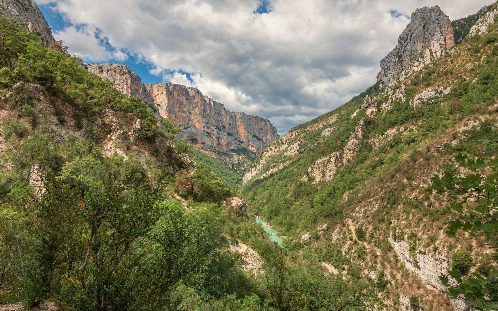 Steep limestone cliffs rise above a turquoise river winding through a forested gorge