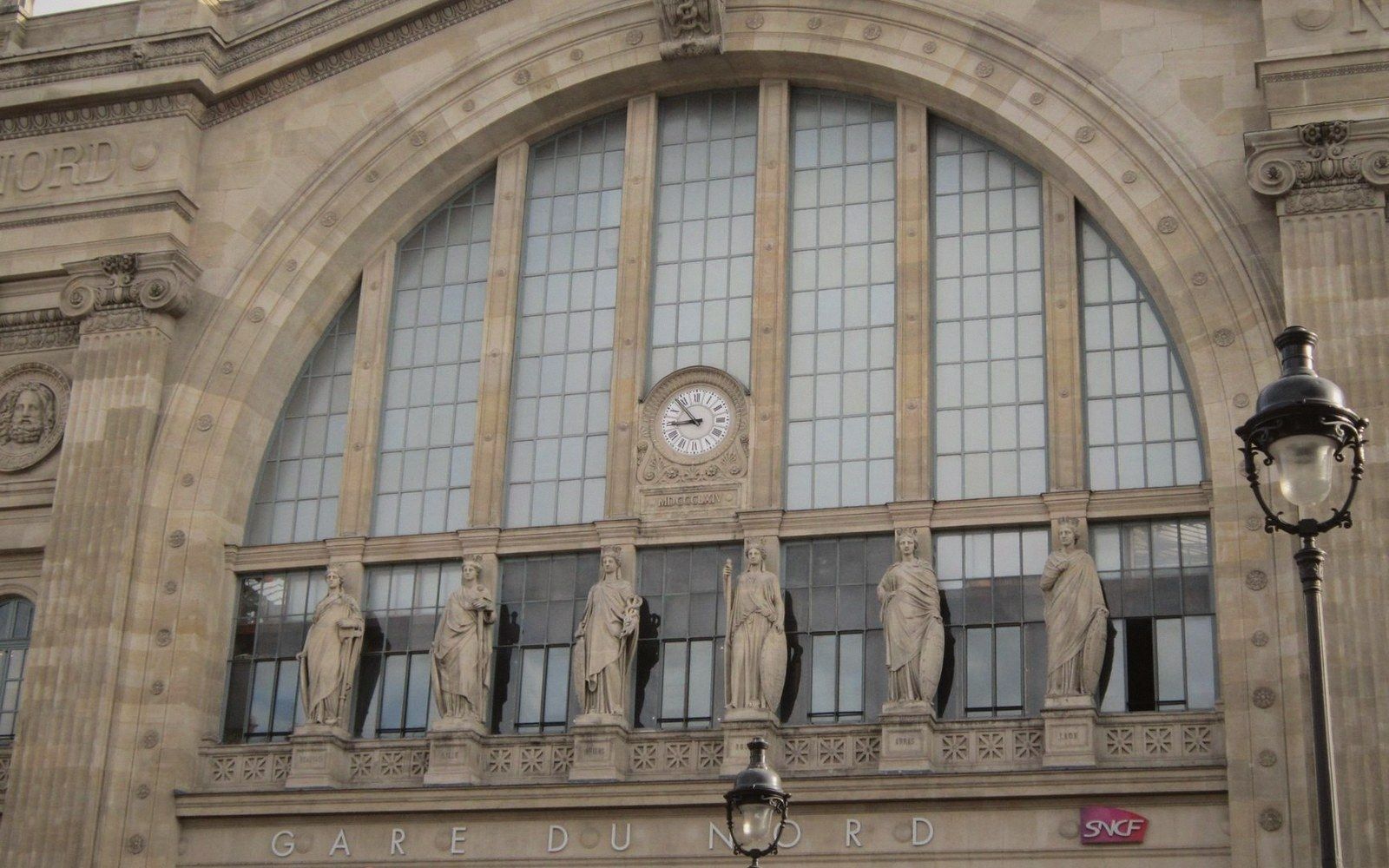 Statues line the arched facade of Gare du Nord beneath a large clock and windows