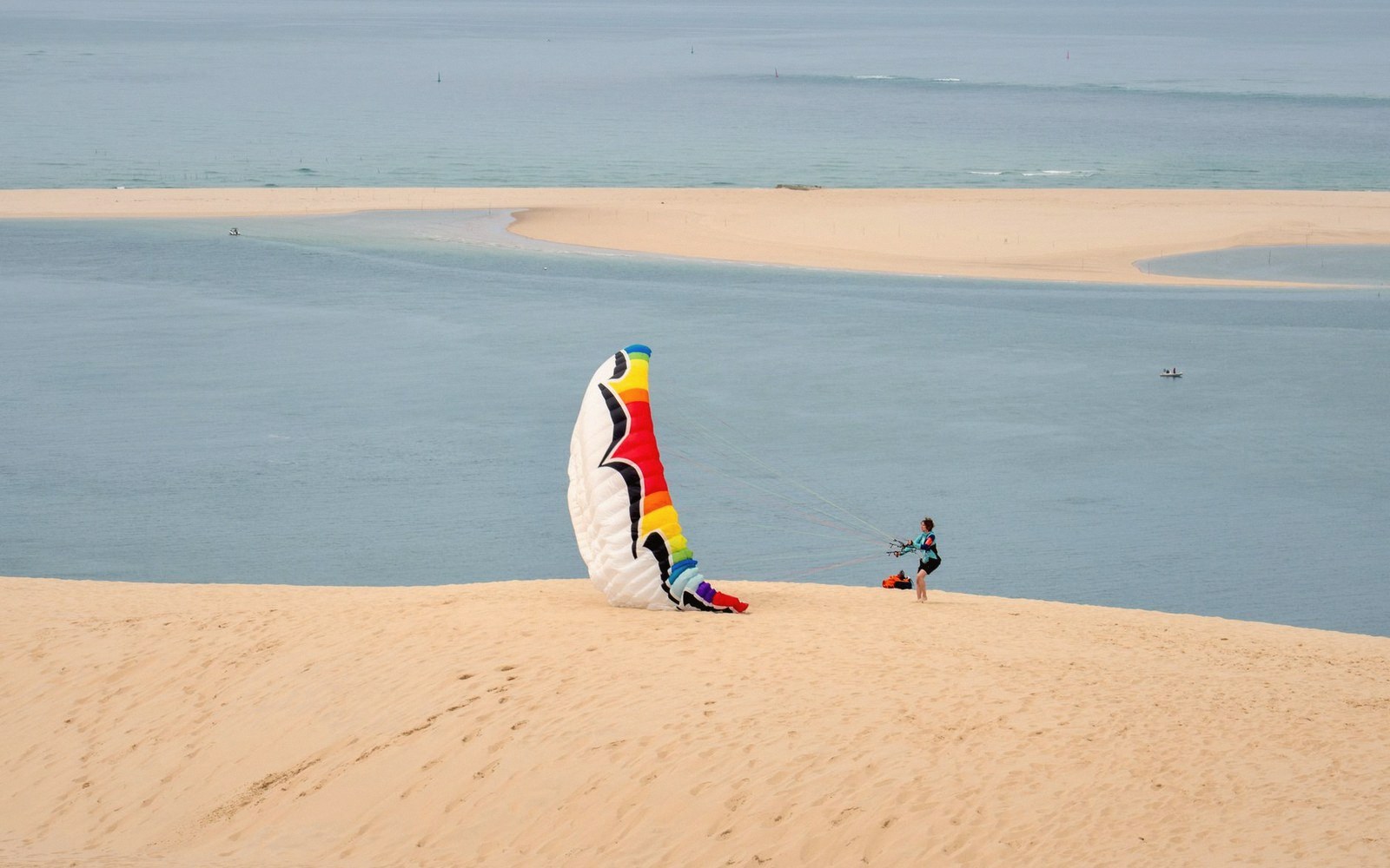 A paraglider prepares their colorful wing atop a sand dune overlooking the coastline
