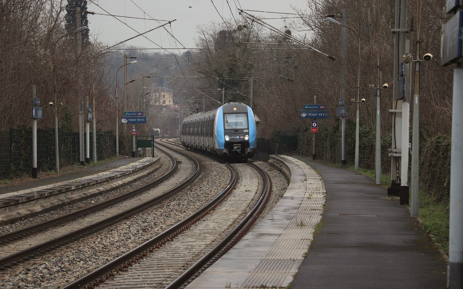 A regional train approaches a curved platform along overhead electrified tracks