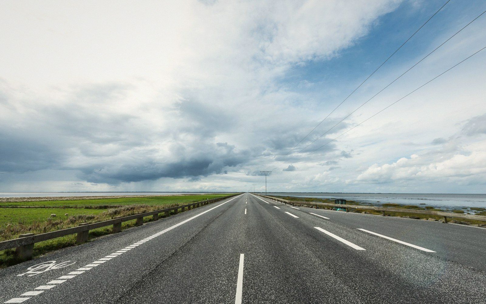 Empty causeway road stretching toward the horizon between flat coastal marshland and open water