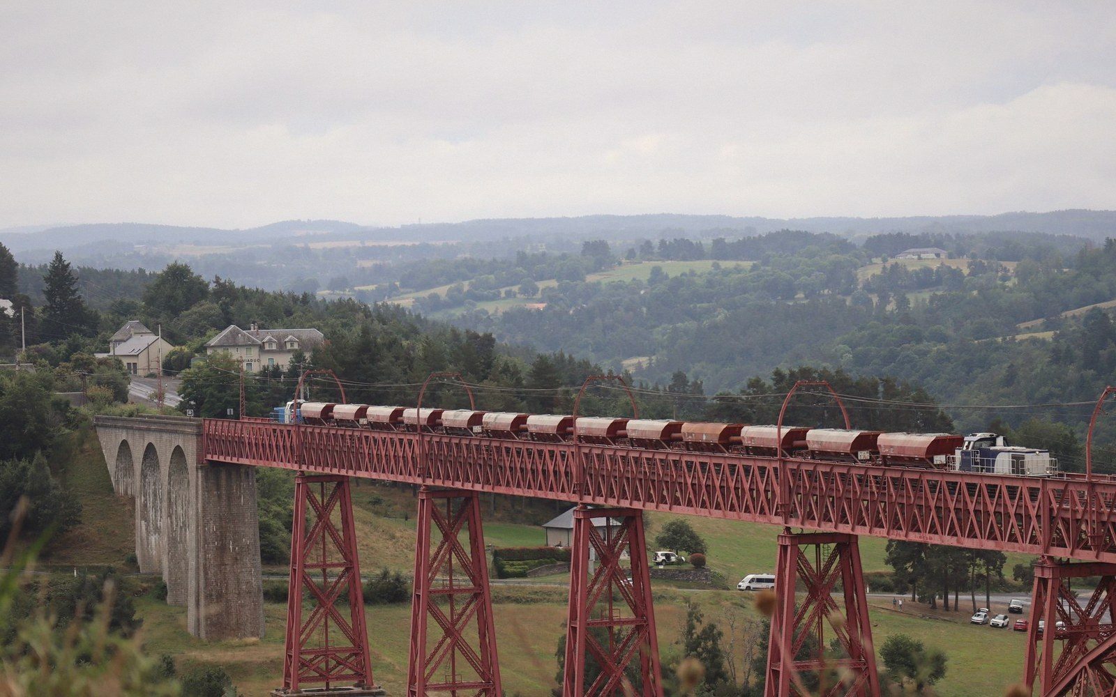 A regional TER train crossing a stone railway viaduct in the French interior, green valley below, overcast sky